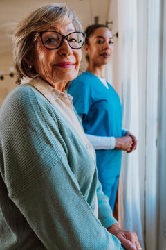 Elderly woman with caregiver in blue scrubs receiving assistance at home