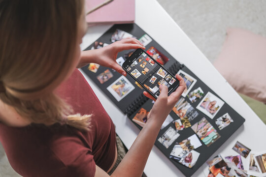 Woman photographing a handmade photo album with a smartphone indoors
