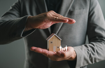 Naklejka premium Businessman hands protect wooden house model and family icon. Real estate insurance, home security, and financial property protection concept for mortgage loan, investment safety, and life assurance.
