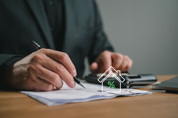 Naklejka premium Businessman using calculator and writing on document with house interest rate icon. Concept of real estate tax, mortgage loan calculation, financial planning, and home property investment.
