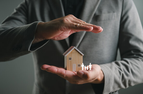 Businessman hands protect wooden house model and family icon. Real estate insurance, home security, and financial property protection concept for mortgage loan, investment safety, and life assurance.