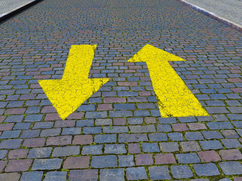 Yellow arrows pointing in opposite directions on cobblestone street