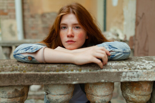 Pensive teenage girl with red hair leaning on a stone balustrade