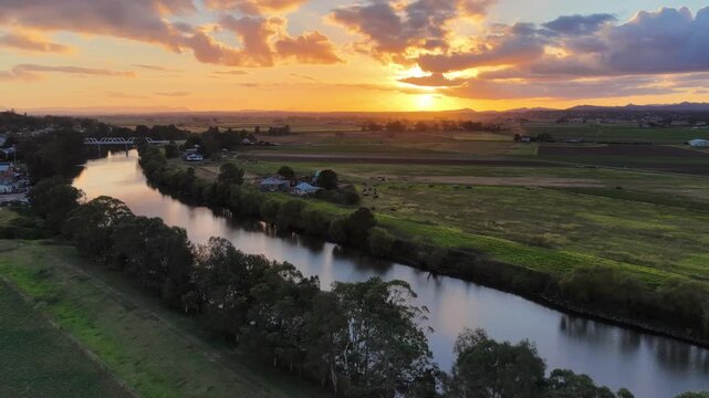 Aerial video flying over the Hunter River in Morpeth in NSW, Australia towards sun setting over farmland. Scenic rural landscape showing river, agricultural fields and warm evening light.
