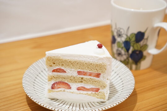 いちごショートケーキのカット断面と花柄マグカップ、カフェ風のおやつシーン