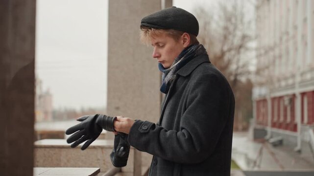 Man preparing gloves. Individual inspecting leather gloves against muted city backdrop for content. Closeup of person preparing leather gloves with focused expression in autumn city environment