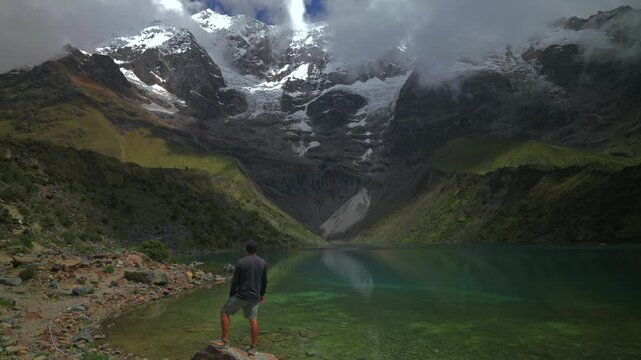 Peru's Laguna Humantay glacial Lake Humantay rocky shoreline tourist people Peruvian Andes Mount Humantay Peru nature landscape view snow covered peaks fog cloud layer morning sunny cloudy static