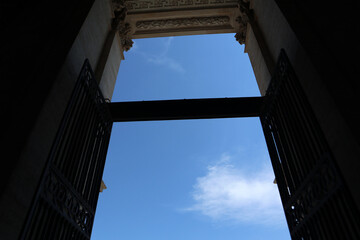 Prospettiva dal basso del grande portone aperto in ferro battuto della Basilica di San Giovanni in Laterano che incornicia un cielo azzurro limpido con nuvole, Roma, Italia. © Ilarialapreziosa