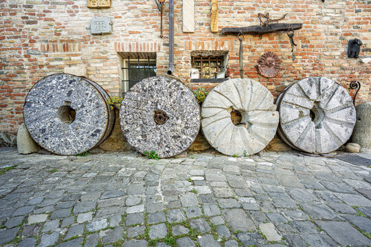 Old stone millstones displayed against a rustic wall in the village of Mondaino, Emilia‑Romagna, Italy