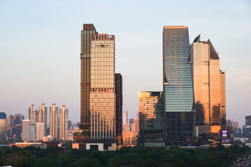 Fototapeta premium An aerial view from Dusit Central Park in the evening, a favorite landmark for tourists and travelers. The sunset casts its light reflecting off the tall buildings surrounding Lumpini Park