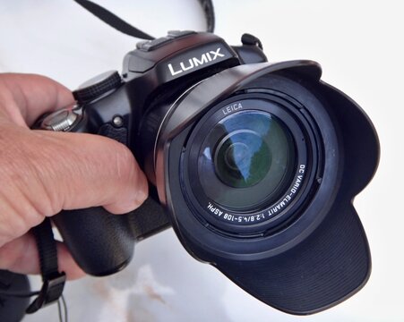 Hand holding Panasonic Lumix Leica camera with lens hood