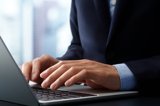 Businessman using laptop computer at desk in office. Closeup of hands and keyboard. Business technologies.
