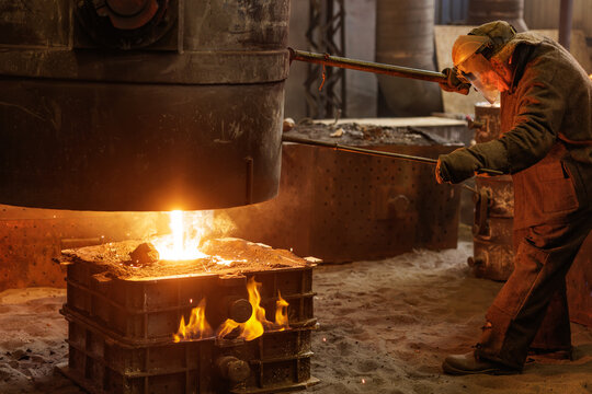 Industrial worker pouring molten metal in foundry mold