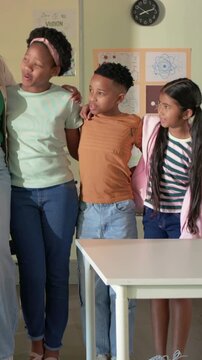 Teacher placing arm around student, students linking shoulders, smiling at camera in classroom
