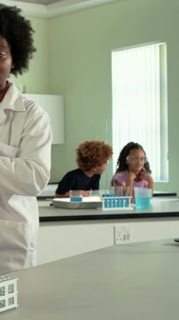 Science teacher arranging green tubes into rack, raising flask while teaching chemistry class