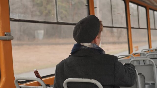 Elderly white creator sitting on tram, gazing through foggy window at autumn field wearing beret and scarf, umbrella beside seat, empty rows and muted vintage interior create contemplative mood