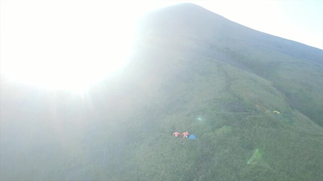 Aerial view of tents on a mountain ridge during a misty sunrise hiking adventure.
