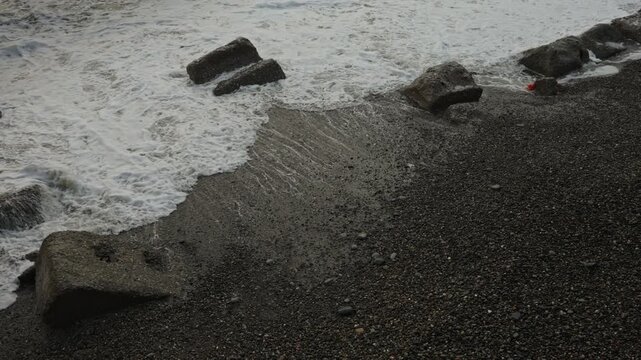 Receding waves revealing patterned pebble shore, coastal engineer inspection, flowing foam, wet stones, tranquil aftermath, muted