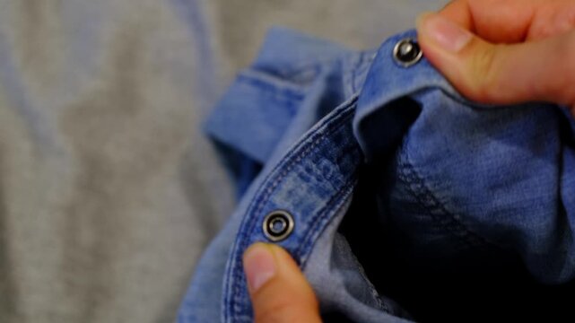Close up shows hands unsnapping metal buttons on a denim shirt laid flat, fabric texture sharp in soft indoor light. Simple wardrobe routines save time, reduce stress, and support mindful consumption.