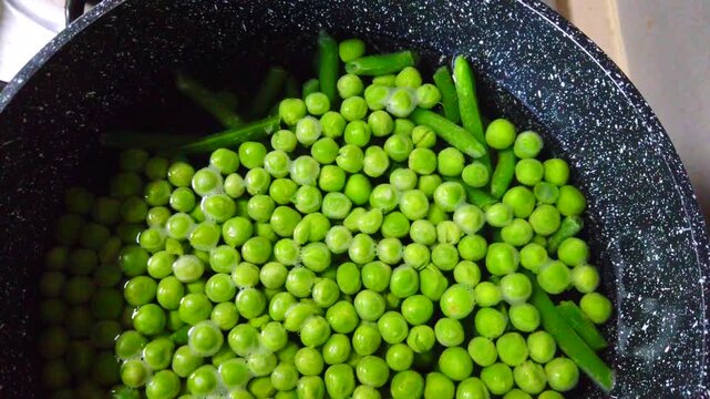 Fresh green peas and broad beans cooking together in a saucepan. A simple and healthy food preparation scene, ideal for vegetarian recipes, meal prep, and kitchen visuals.