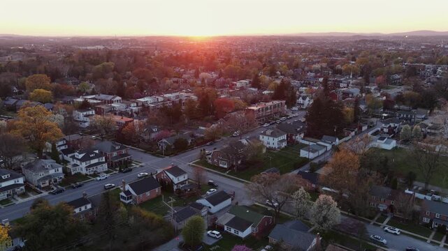 Charming small American city at sunset with row houses, neighborhood streets, spring trees and glowing cityscape in Pennsylvania, showing peaceful suburban blocks and evening light. Aerial drone wide