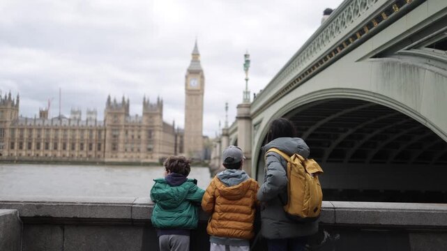 Mother with two young sons enjoying the iconic view of big ben and the houses of parliament from the river thames embankment on a cloudy day in london, united kingdom