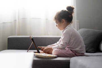 Young girl using tablet at home in natural light, early childhood technology and education concept © chandlervid85