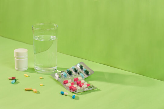 Medication pills, capsules, and glass of water on green background