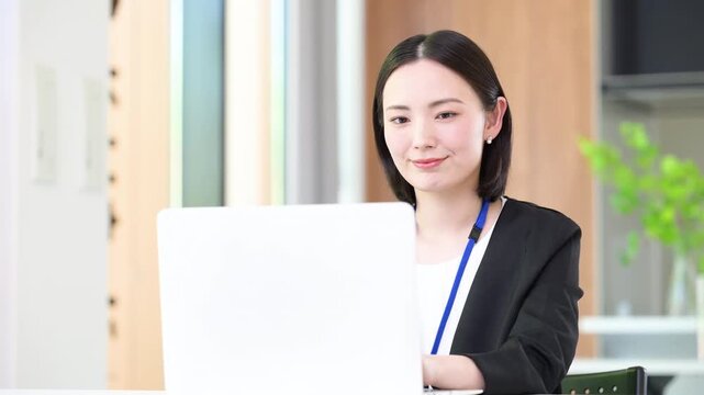 ノートパソコンを前に仕事をする名札ををつけたタイピング笑顔の女性会社員 オフィスワークのイメージの動画