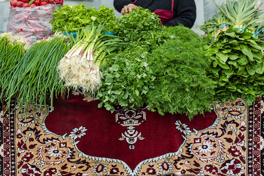 Fresh herbs and greens displayed on a traditional carpet at Siab bazaar in Samarkand. Bunches of dill, cilantro, and spring onions create a vibrant market scene ideal for travel and food content.