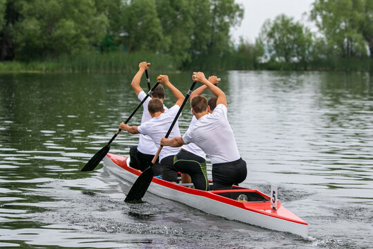 Rear view four athletes canoeist paddling on open water