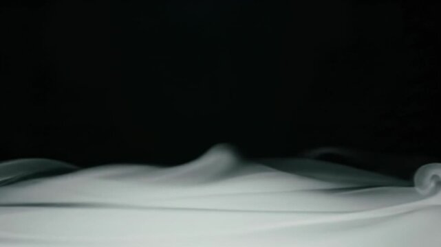 ethereal white smoke and translucent fog billow slowly across a stark deep black void background in a static wide-angle video with soft backlighting. Serene abstract ambiance concept