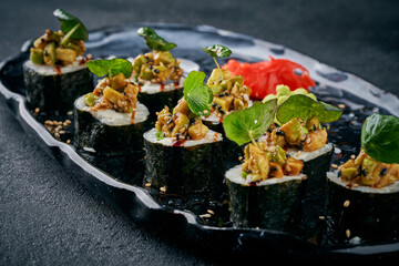 Delicious sushi rolls topped with spicy tuna or nut mixture and parmesan sprinkles, served with ginger and wasabi on a black plate © ismishko