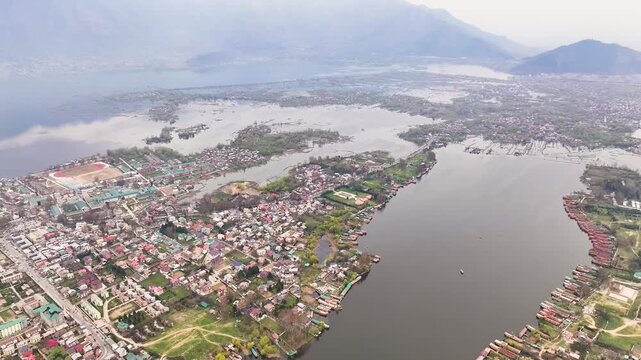 Cinematic wide aerial pullback over Srinagar, revealing the immense scale of Dal Lake, dense urban settlements, waterways, houseboats, and the towering Himalayan mountain range in Kashmir.
