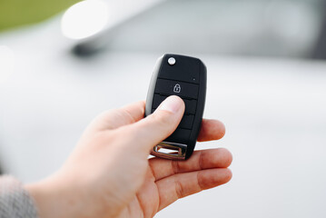Fototapeta premium black car keys in woman hand, close-up view, white car in background, opening or closing car with signalization or alarm system, car theft, carjacking, car safety concept, selective focus