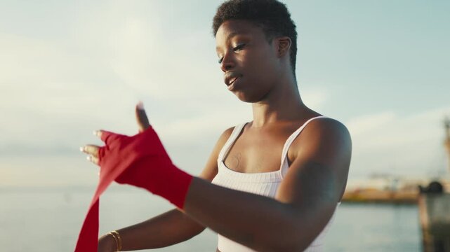 Black woman fighter wrapping hands with red bandages outdoors