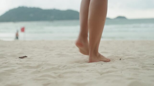Lady explores seaside in warm weather. Woman enjoying leisurely stroll amid beach crowd and scenic views. Female visitor casually walks on sunny island beach among tourists and distant landforms