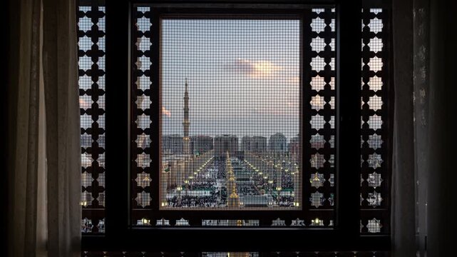 Day to night timelapse of the Prophet's Mosque in Medina, Saudi Arabia and all the people visiting the religious site. Seen through a hotel window