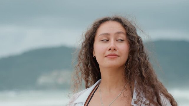 Gleeful woman with curly hair enjoys island view. Cheerful lady with curly locks admires serene islandscape. Joyful woman with curly hair and soft smile takes in peaceful island scenery