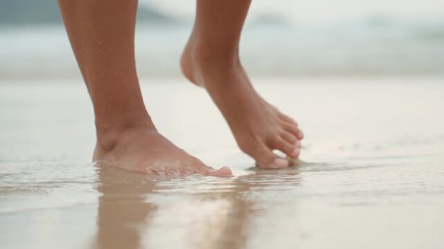Bare feet walking along island shore, soft wet sand, gentle waves lapping, reflective puddles near ankles, meditative mood, morning walker, yoga practitioner, beachcomber, casual traveler