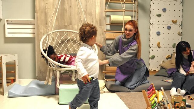 Toddler boy playing while teacher gently rocks sleeping girl