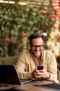 Smiling Man Working Remotely on Laptop and Phone at Outdoor Cafe, Casual Business Lifestyle