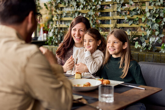 Happy Mother and Two Daughters Laughing Together at Restaurant Family Dining and Bonding Moment