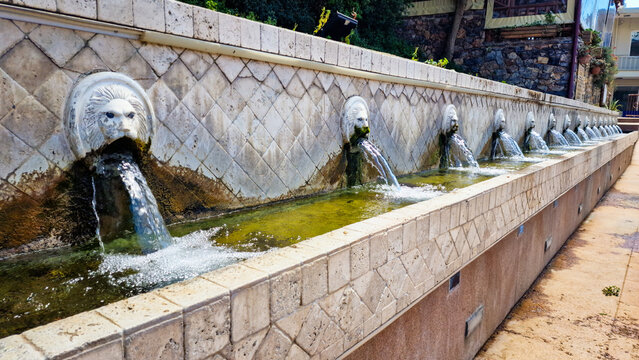 Panoramic view of Venetian lion head fountains in Spili village, Crete. Row of ancient stone sculptures with fresh mountain spring water. Historic Greek heritage in Rethymno, high resolution