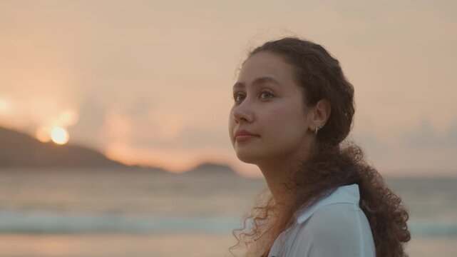 Young woman island beach sunset gazing ocean, soft golden hour light, distant island silhouette, contemplative side profile, flowing curly hair, subtle earring, relaxed cardigan, gentle waves,
