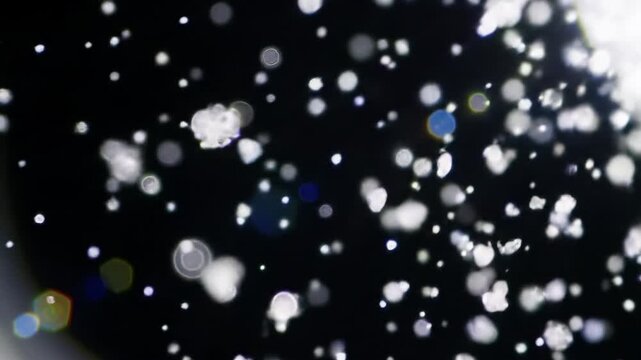 extreme macro video: translucent dust particles drifting in a black void, softly lit with volumetric light and a slow push-in. Ethereal, meditative concept