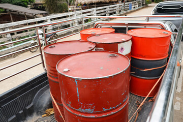 Red metal oil barrels loaded in back of pickup truck with metal rails parked on dirt road outdoors in rural industrial area conveying sense of heavy labor and practical transportation © CoreRock