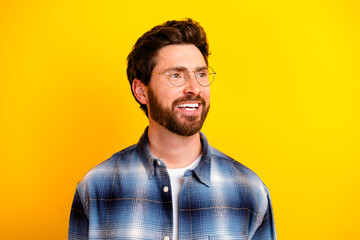 Obraz premium Smiling bearded man wearing glasses and a plaid shirt looking away against a bright yellow background, casual portrait conveying happiness and confidence