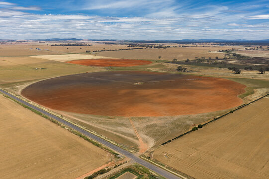 Aerial view of ploughed circular paddock alongside a country road under a blue sky