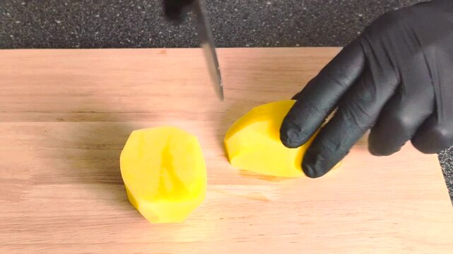 Slicing peeled potato on wooden cutting board with knife. Close up food preparation.